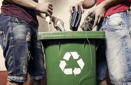two people recylcing electronics into a bin