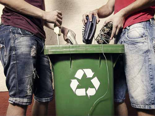two people recylcing electronics into a bin