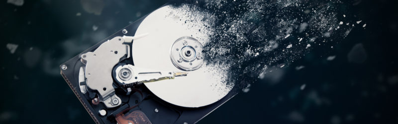 A hard drive with particles of data disintegrating and floating away from it, symbolizing data destruction.