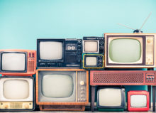 A collection of vintage televisions of various sizes and styles, stacked on top of each other