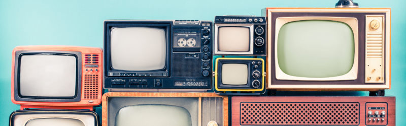 A collection of vintage televisions of various sizes and styles, stacked on top of each other