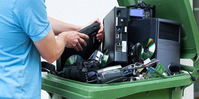 Man discarding old cds and dvd players in a recycling bin