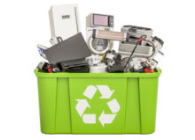 A green recycling bin with a bunch of electronics in it